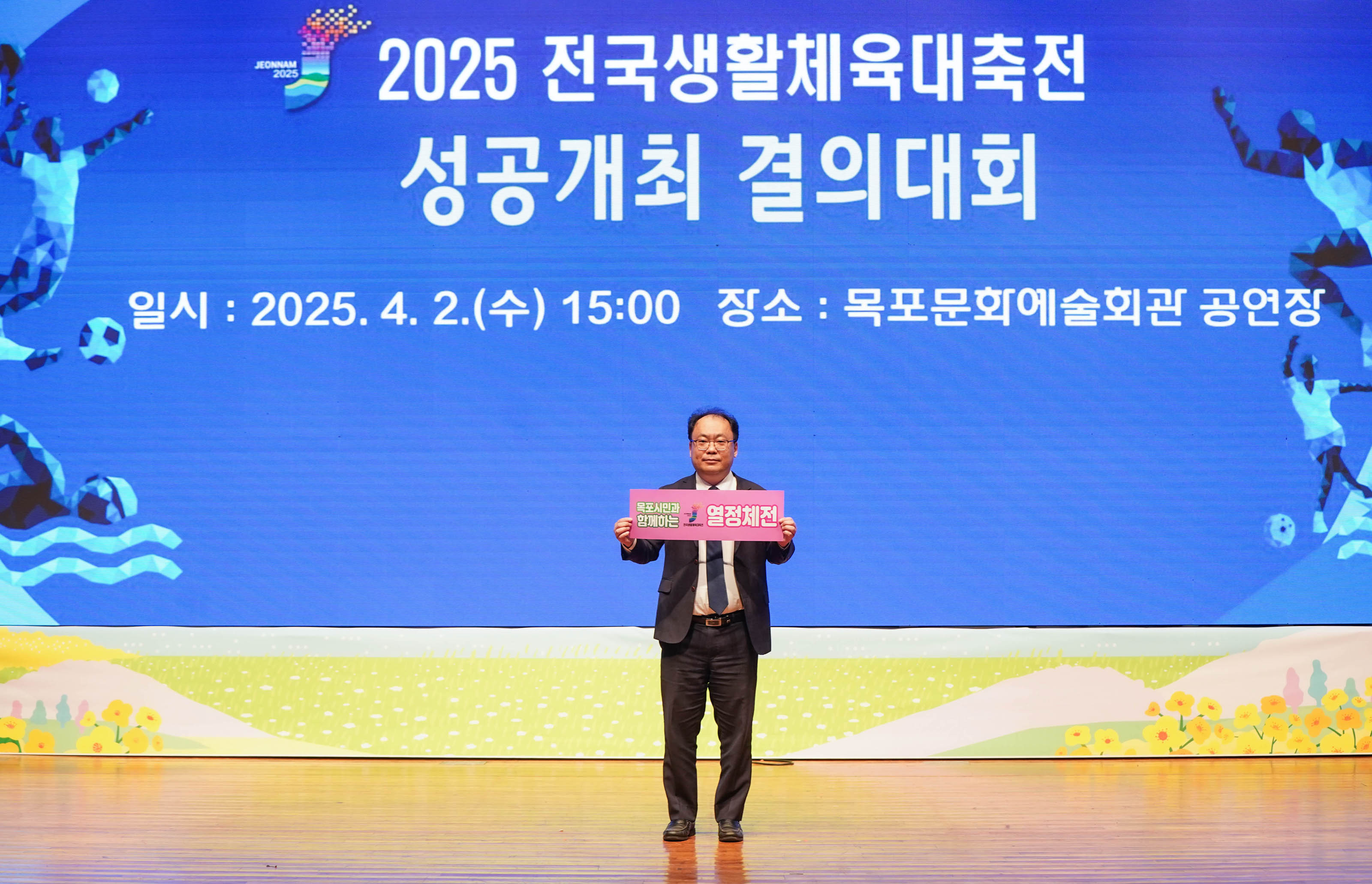'2025 전국생활체육대축전
성공개최 결의대회
일시:2025.4.2.(수) 15:00 장소: 목포문화예술회관 공연장' 문구가 띄워진 스크린 앞에서 '열정체전' 문구가 적힌 팻말을 든 관계자의 모습