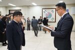 2026년 상반기 4급이하 정기인사로 정장을 입고 안경을 쓴 남성이 실내 행사장에서 한 남성에게 상장을 전달하며 내용을 읽고 있고, 남성은 안경을 쓰고 어두운 자켓을 입은 채 서 있으며 뒤쪽에는 여러 사람들이 줄지어 서서 행사를 지켜보고 있다.